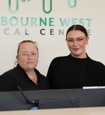 Doctors at Cranbourne West Medical Centre standing at reception with the clinic logo wall
